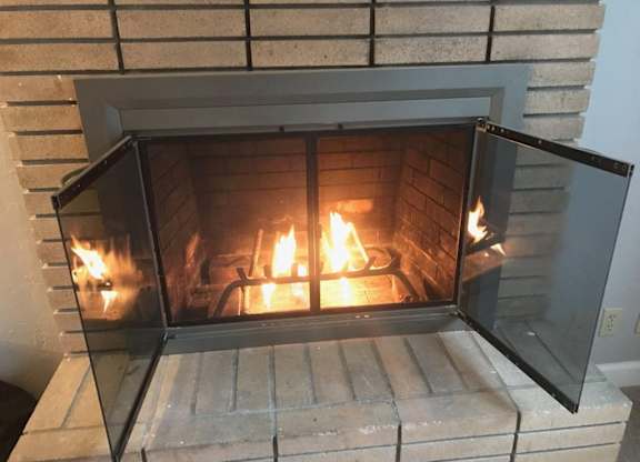 A fireplace with a glass door open, showing a fire burning inside.