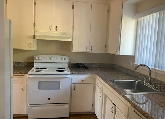 A white stove is in a kitchen with white cabinets.