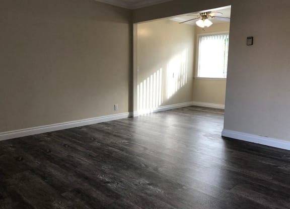 an empty living room with wood floors and a ceiling fan