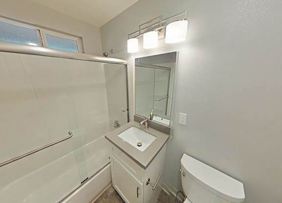 A white bathroom with a sink, mirror, and toilet.