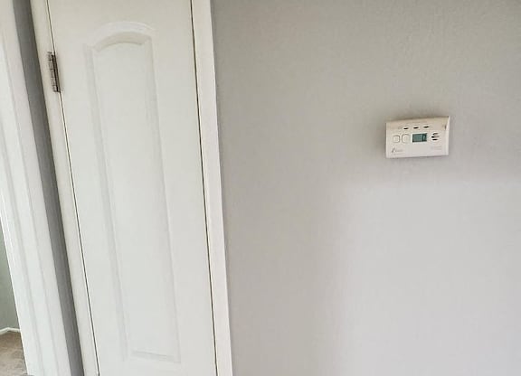 A white door with a white wall and a thermostat on the wall.