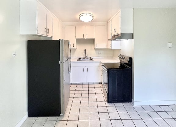 an empty kitchen with white cabinets and a black refrigerator