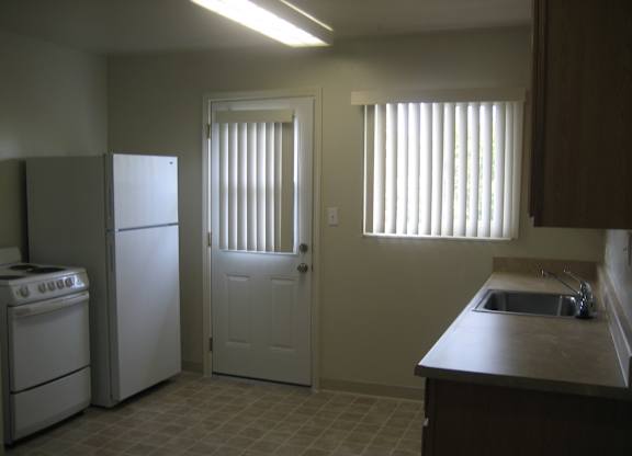 A kitchen with a white refrigerator, a white oven, and a white door.