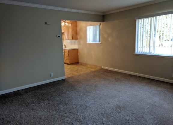 an empty living room with a kitchen in the background