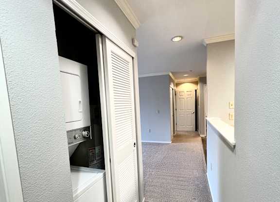 A narrow hallway with a white door on the left and a carpeted floor.