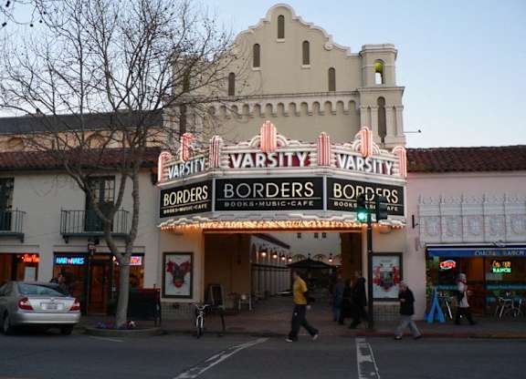 a theater on the corner of a street with people walking