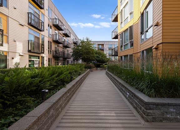 A long wooden walkway leads between two rows of modern apartment buildings.