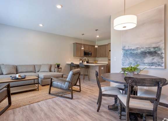 A modern living room with a grey sofa, a wooden dining table and chairs, and a kitchen area in the background at Ventura Townhouses, Michigan