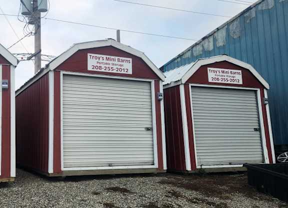 Three mini barns with red and white colors and the name Troy's Mini Barns on them.