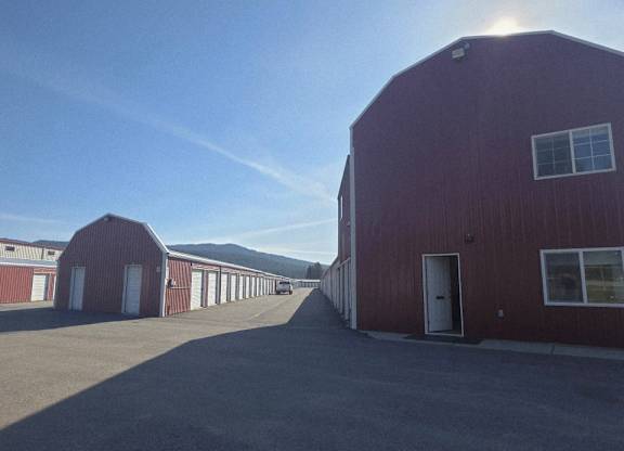 A red barn with a white door is in the foreground of a sunny day.