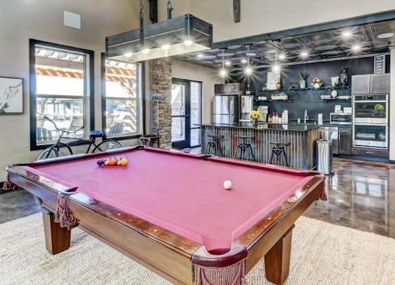 A pool table in a room with a kitchen in the background.