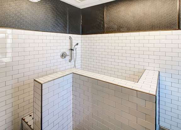 A white tiled shower with a silver faucet.