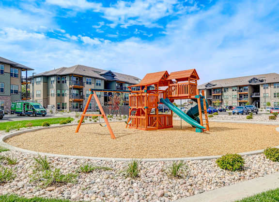 A playground with a slide and a swing set in front of apartment buildings.