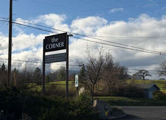 A sign for "The Corner" is displayed in front of a rural landscape.