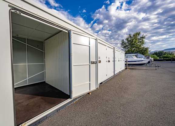 A white shipping container is open with a boat in the background.