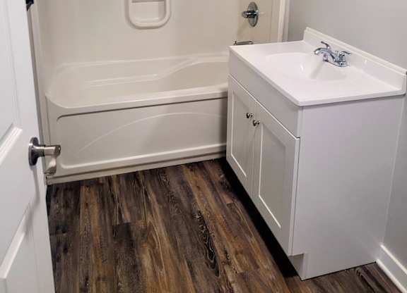 A white bathroom with a wooden floor and a white sink.
