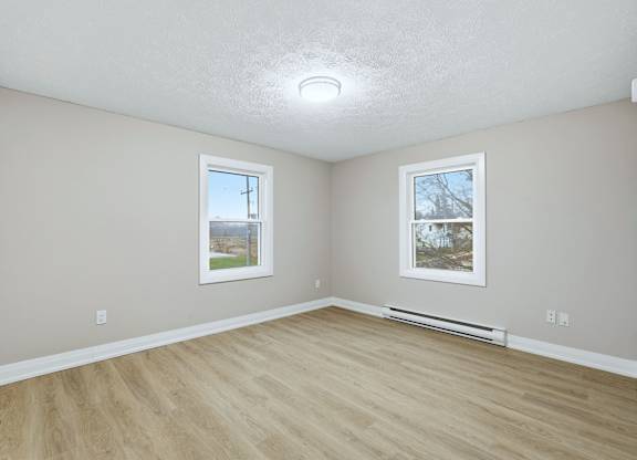 A room with light wood flooring and two windows.