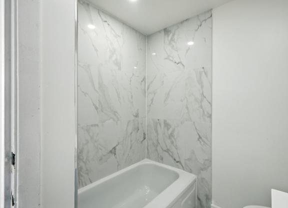 A white bathroom with a marble wall and a white tub.