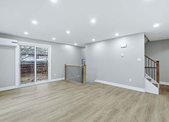 A spacious room with a wooden floor and a staircase on the right side.
