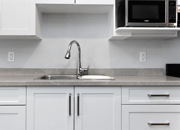 A kitchen with white cabinets and a black microwave above the sink.