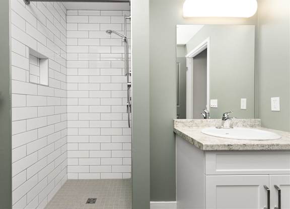 A bathroom with a white tiled shower and a sink with a marble countertop.