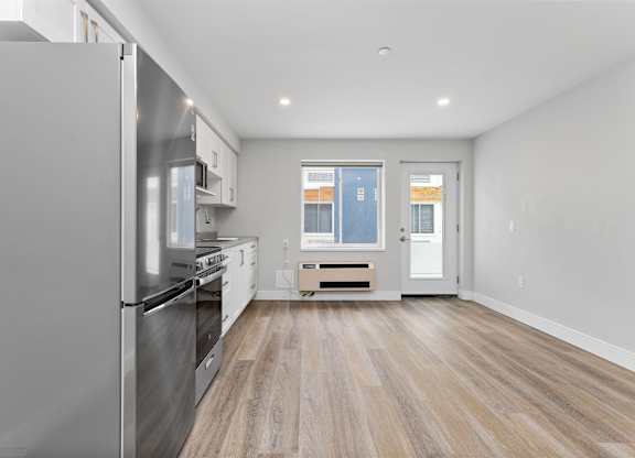 A kitchen with a stainless steel refrigerator and wooden flooring.