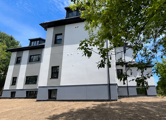 A white building with a black roof is surrounded by trees.