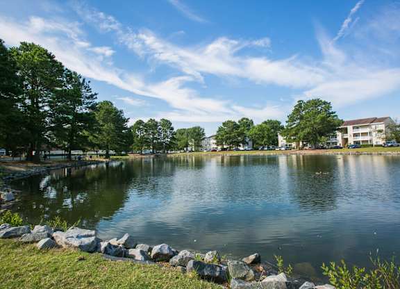 A serene lake surrounded by trees and a building in the distance under a clear blue sky.