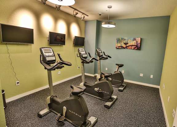 A gym room with exercise bikes and a television.