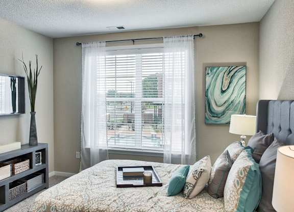 A bedroom with a large bed, a nightstand, and a window with blinds.