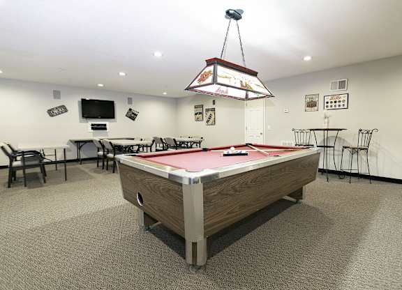 A pool table is in the middle of a room with a television and pictures on the wall.