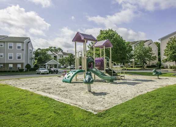 A playground with a purple and green slide in the middle of a grassy area.