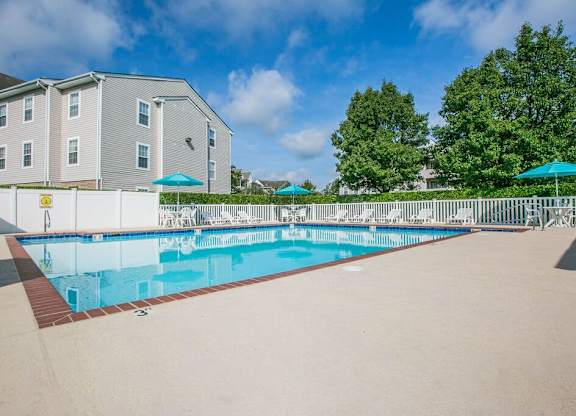 A swimming pool in front of a grey building with trees in the background.