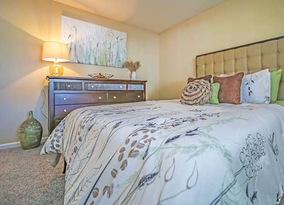 A bed with a white comforter and a green vase on the floor.