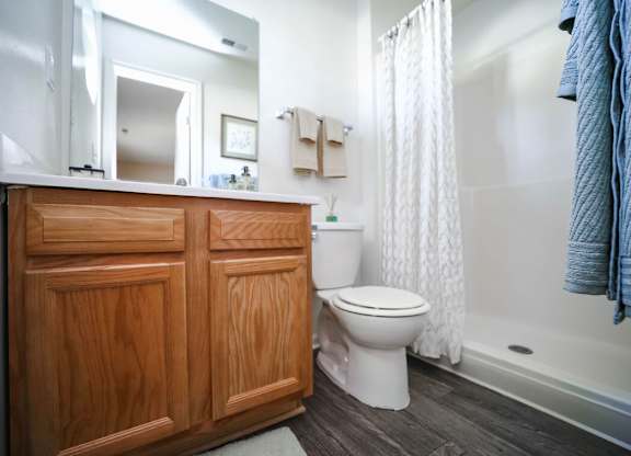 A white toilet sits in a bathroom with a wooden cabinet and a white shower curtain.
