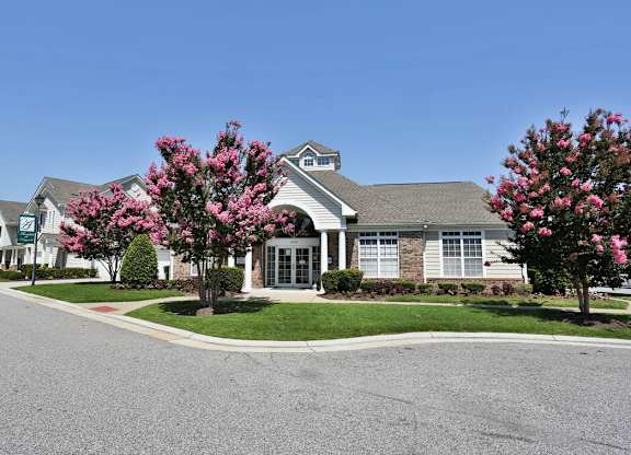A building with a grey roof and a tree with pink flowers in front.