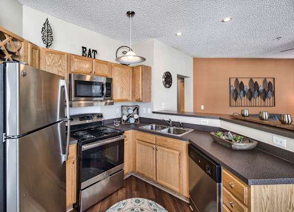 A kitchen with a refrigerator, microwave, oven, sink, and a bowl of vegetables on the counter.