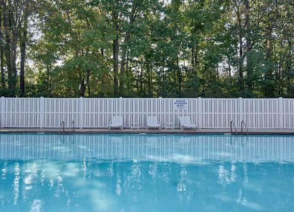 A pool with a white fence and trees in the background.