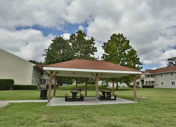 A pavilion with picnic tables is surrounded by grass and trees.