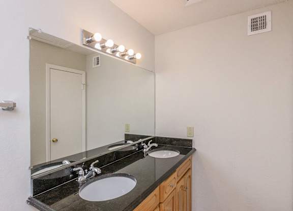 A bathroom with a vanity and a mirror with lights above it.