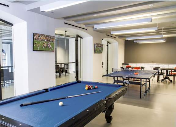 A pool table is in the middle of a room with a mirrored wall.