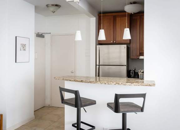 A kitchen with a refrigerator, bar stool and a framed picture on the wall.
