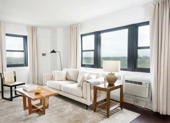 A living room with a white couch, a wooden coffee table, and a large window with a view of the outdoors.