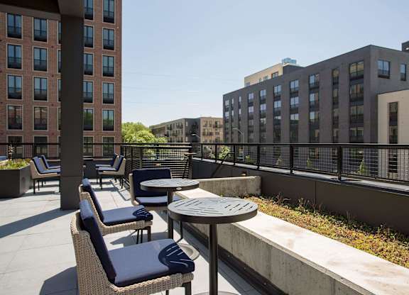 A patio with chairs and tables is surrounded by buildings.