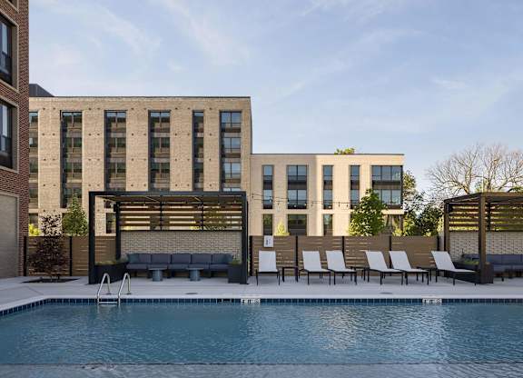 A pool in front of a building with a bench and chairs.