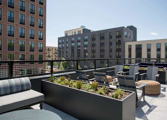 A rooftop patio with a planter box and chairs.