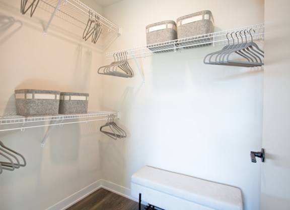 A white closet with clothes hanging on hangers.