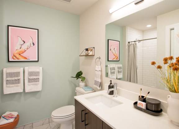 A bathroom with a toilet, sink, mirror, and a vase of flowers.