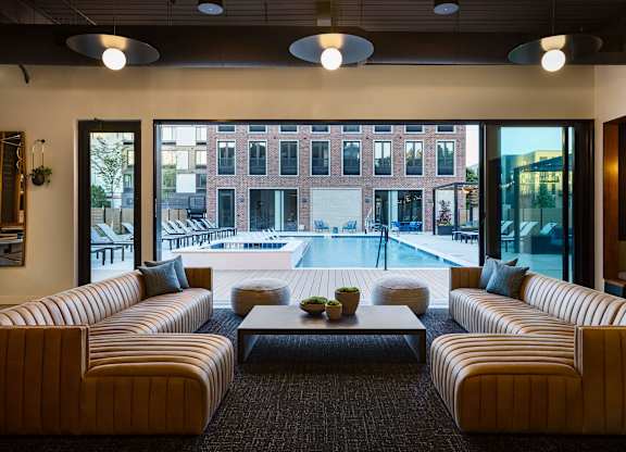 A modern living room with a large window overlooking a pool and buildings outside.