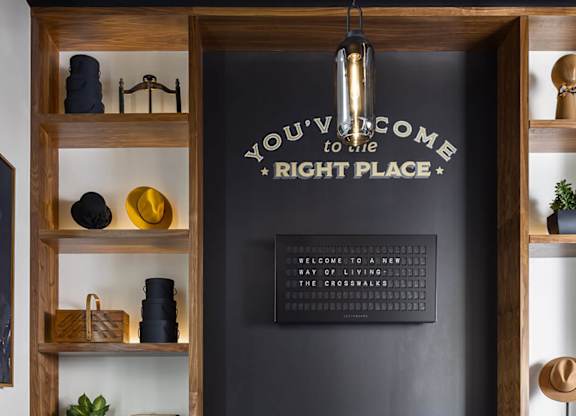 A living room with a grey wall and a wooden shelf with a sign that says "You're welcome to my right place".